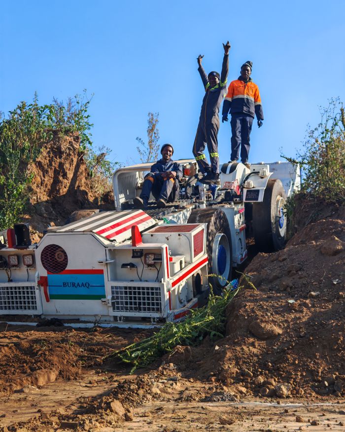 Workers standing triumphantly on mining machinery in Johannesburg, South Africa under a clear blue sky.