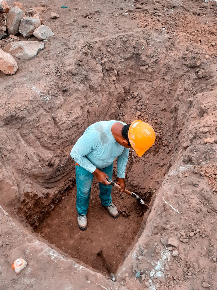 A construction worker in safety gear digs at a site in Lambayeque, Perú, showcasing manual labor and construction processes.